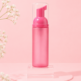 Pink foaming hand soap bottle on a pink background with white flowers.