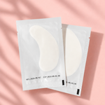 Two pairs of eye cream patches on a pink background