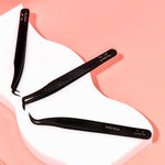 Lash extension tweezers on a white tray with a pink background